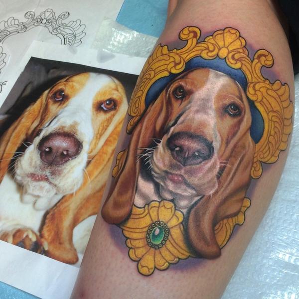 face of Basset Hound inside a gold vintage frame tattoo on the leg