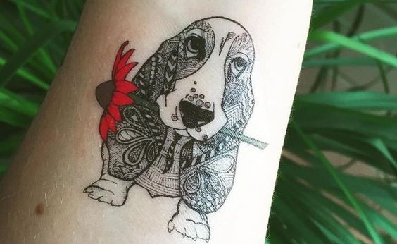 Basset Hound puppy in mandala design with a red flower in its mouth tattoo