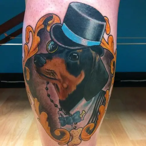Dachshund wearing hat and a one eyeglass in a gold vintage frame tattoo on the leg