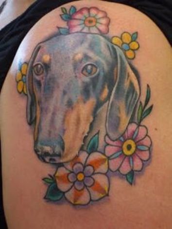 face of a Dachshund surrounded with flowers tattoo on the shoulder