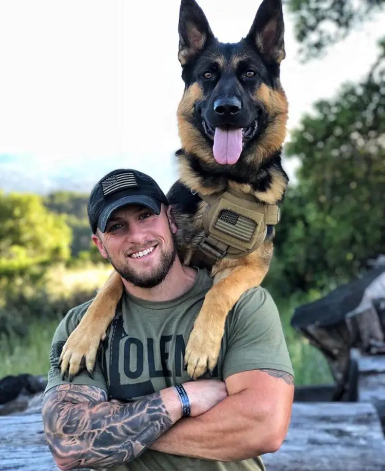 A man with a German Shepherd Dog leaning behind over his shoulders