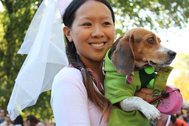 A woman in princess costume carrying a beagle in pea costume