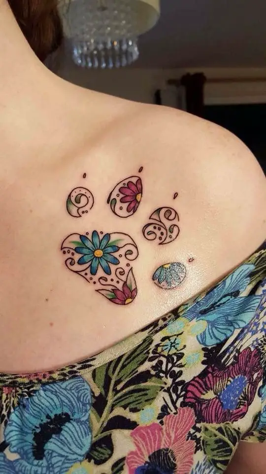 outline of paw print with florals tattoo on the shoulder of a woman