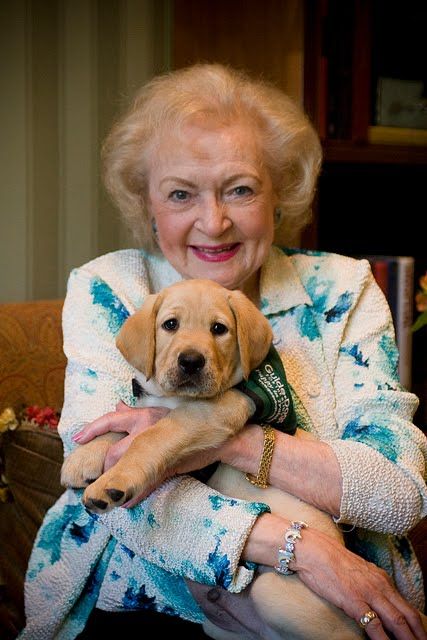 Betty White sitting on the chair while hugging her Labrador Retriever puppy