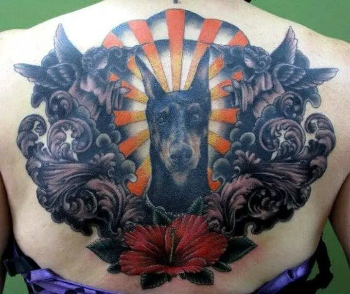 artistic angels and clouds with red flower on the bottom and a Doberman in the middle with ray of sunshine in the background tattoo on the back of a woman