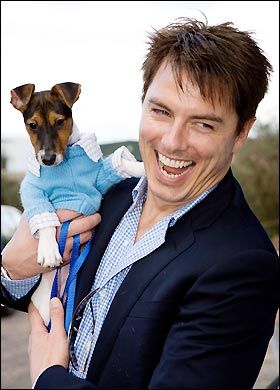 John Barrowman laughing while carrying his Jack Russell Terrier in his arms