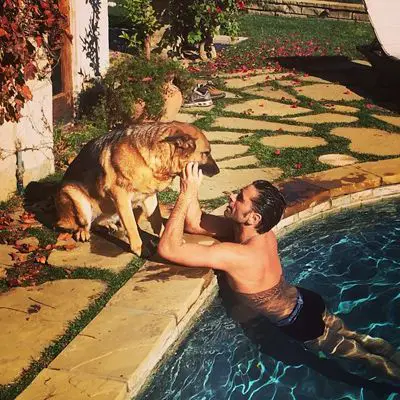John Stamos in the pool while petting his German Shepherd sitting at the pool side