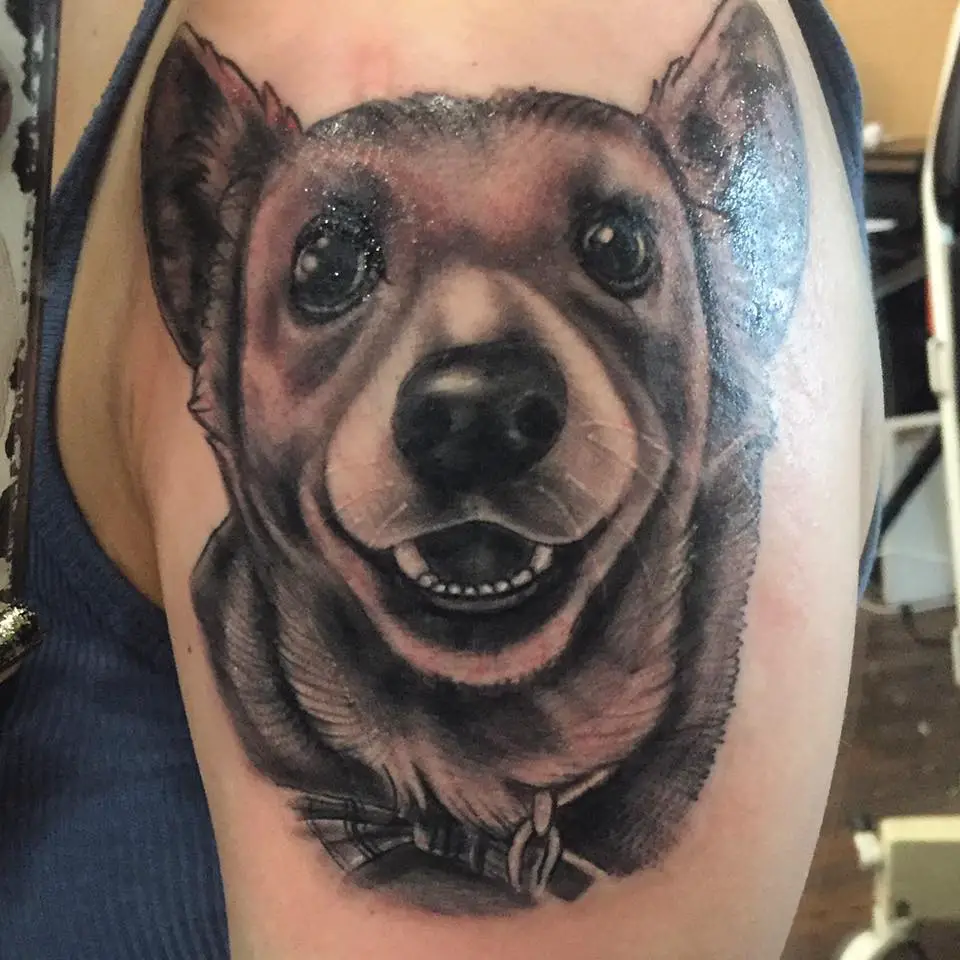 a black and gray happy face of a corgi tattoo on the shoulder of a man