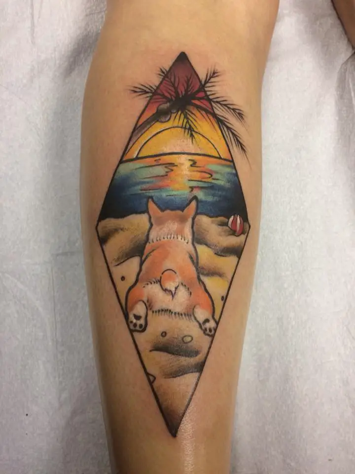 a corgi lying down in the sand at the beach in a diamond shape tattoo on the forearm