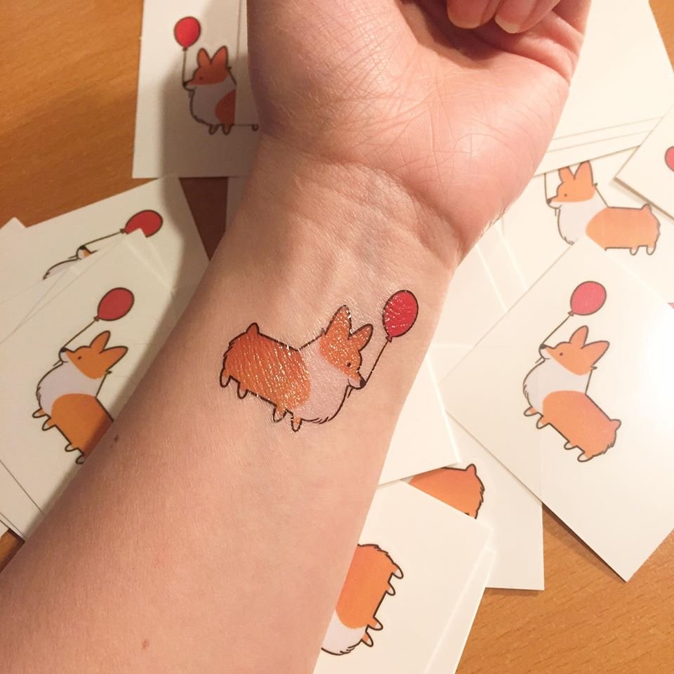 an animated corgi holding a balloon with its mouth tattoo on the wrist