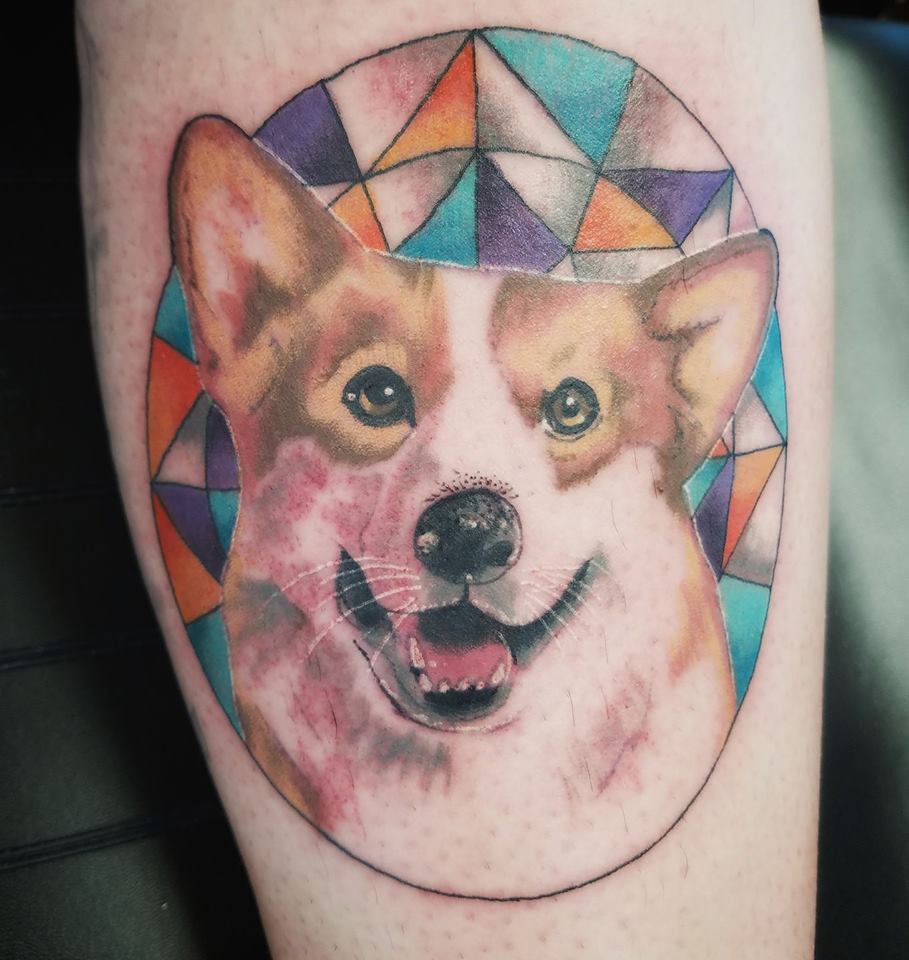 a happy face of a corgi inside a circle with colorful geometric background tattoo on the leg