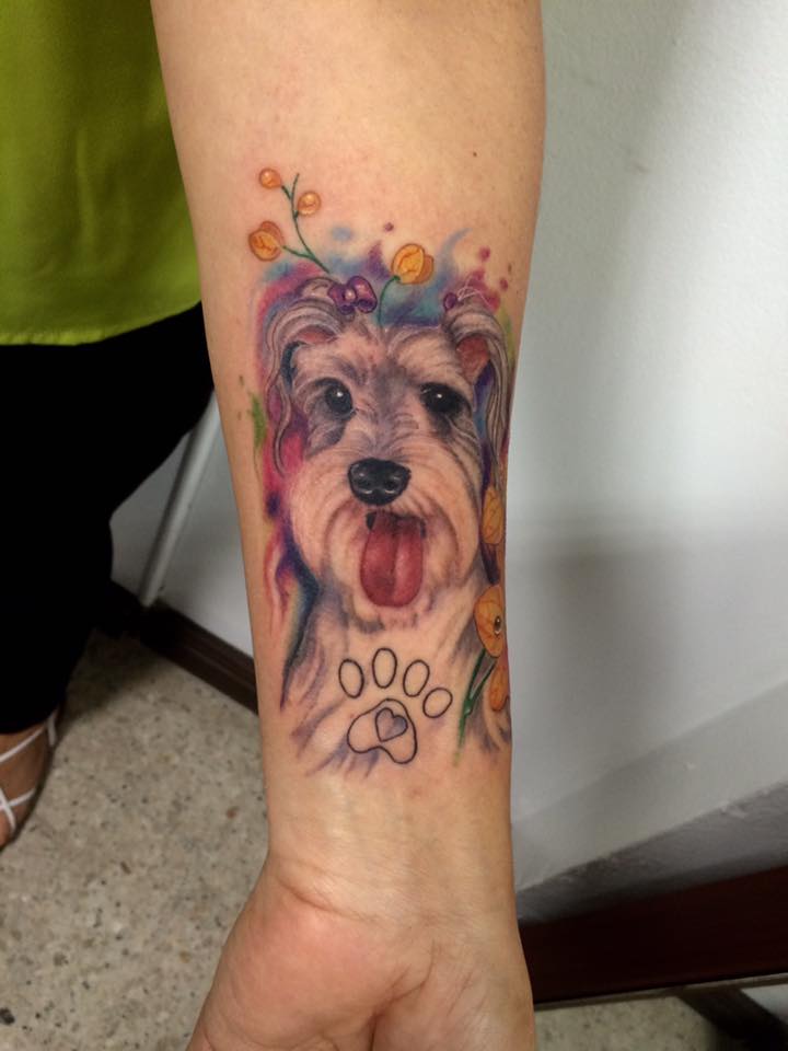 realistic face of Schnauzer with its tongue out with flowers and paw print tattoo on the forearm