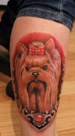 a yorkie in a red shadow and silver frame tattoo on the leg