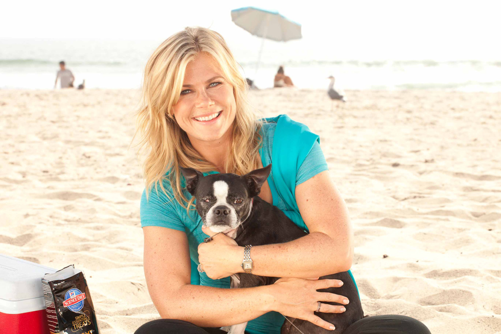 Alison Sweeny sitting at the beach with her Boston Terrier on her lap