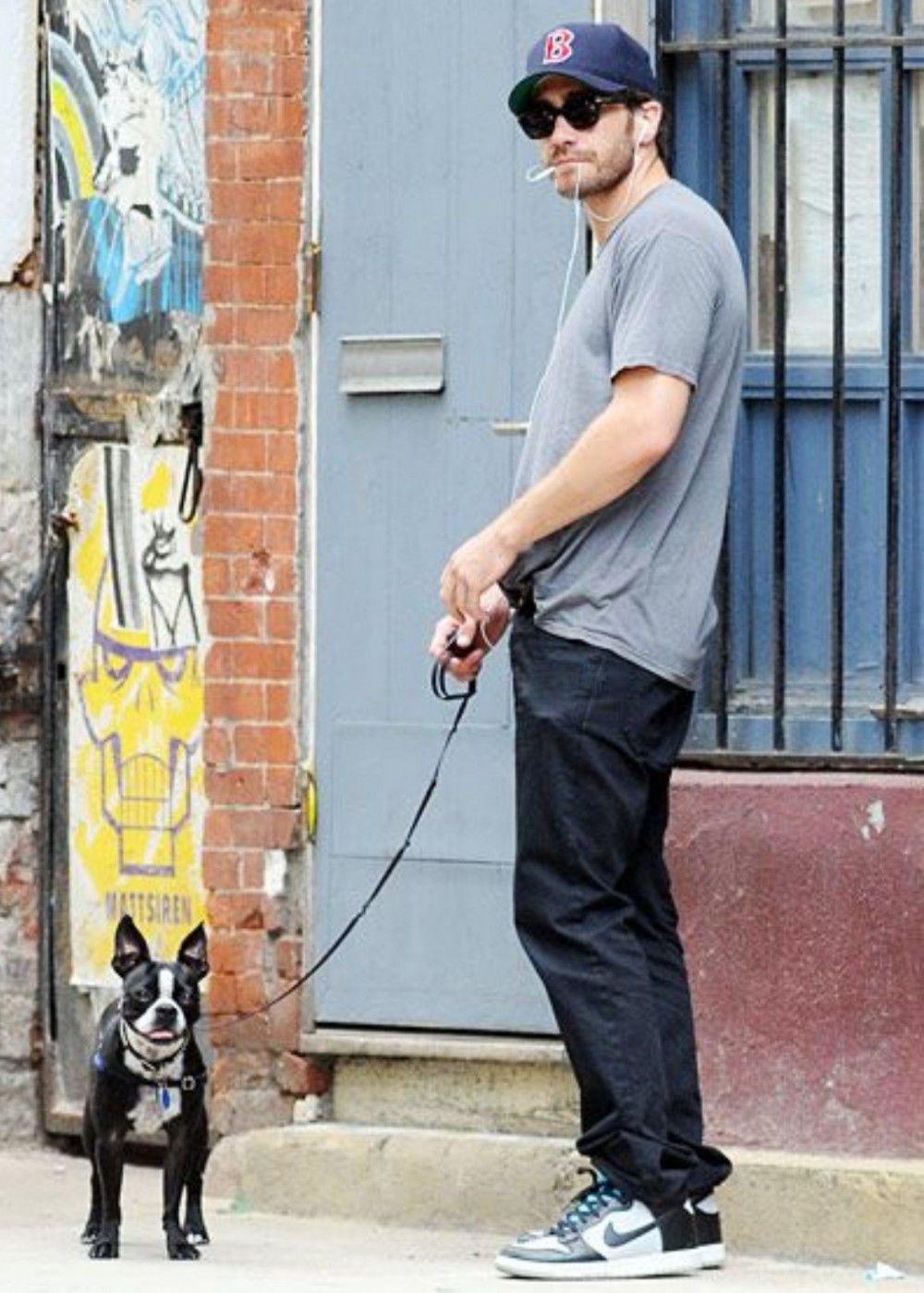 Jake Gyllenhaal standing by the street with his Boston Terrier on a leash standing in front of him