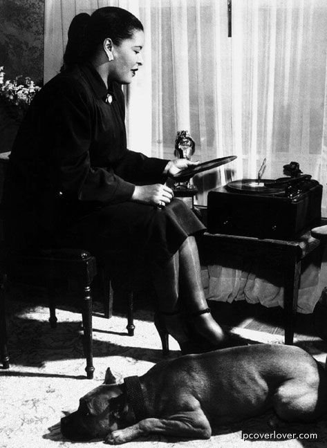 black and white photo of Billie Holiday sitting on the chair while her Boxer dog is on the floor sleeping