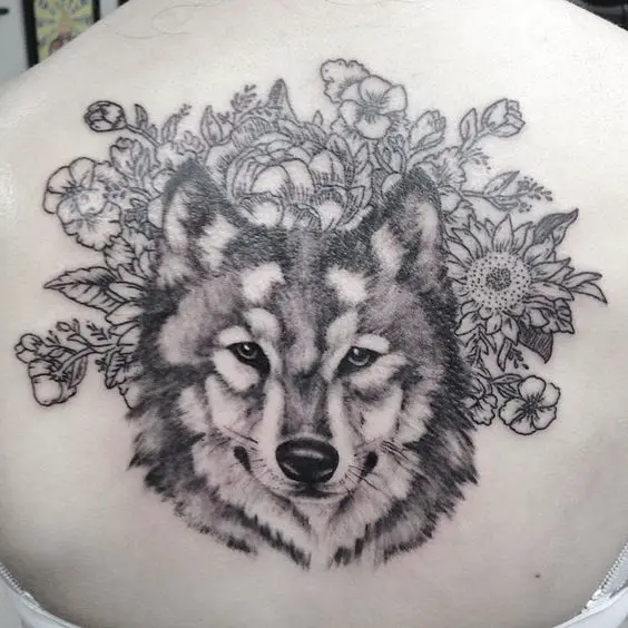 black and gray face of a Husky with flowers and leaves on its background tattoo on the back