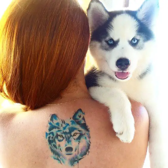 a woman carrying a Husky puppy with its face tattooed on her back