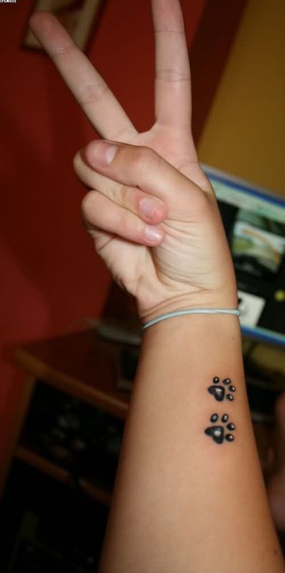 two paw prints tattoo on the wrist of the woman making a peace sign