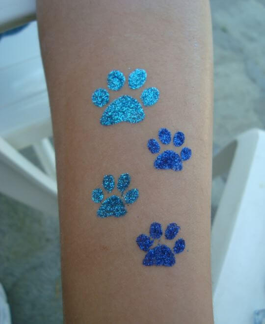 sparkly blue paw prints tattoo on the forearm