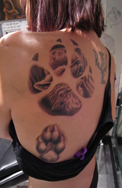 a large paw print with a howling husky design tattoo on the back of the woman