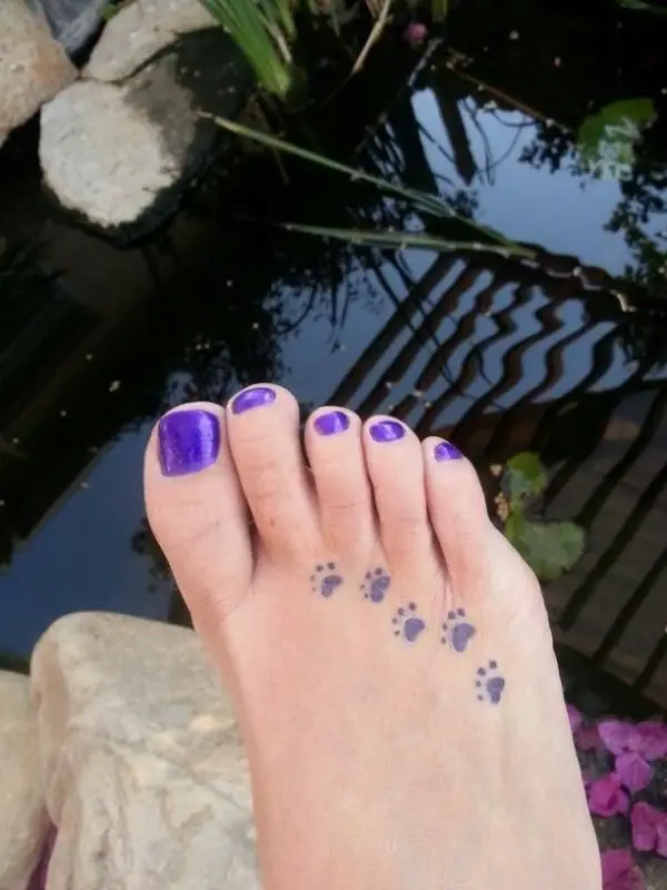 five small paw prints tattoo on the foot of the woman