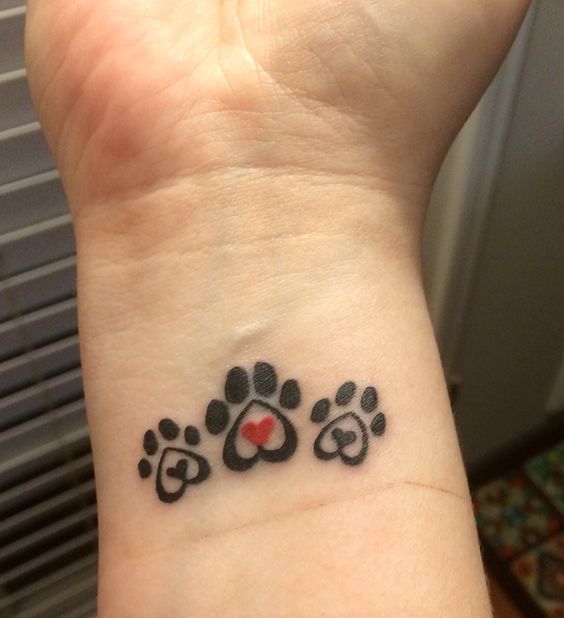 three paw prints with heart in the middle tattoo on the wrist
