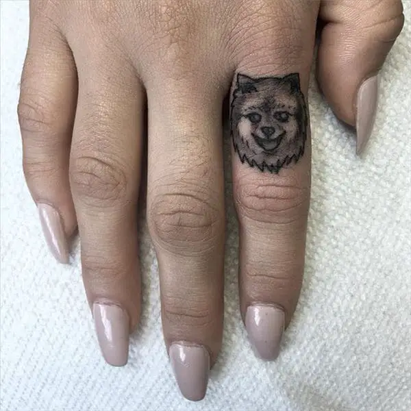 black and gray face of a Pomeranian Tattoo on the pointing finger