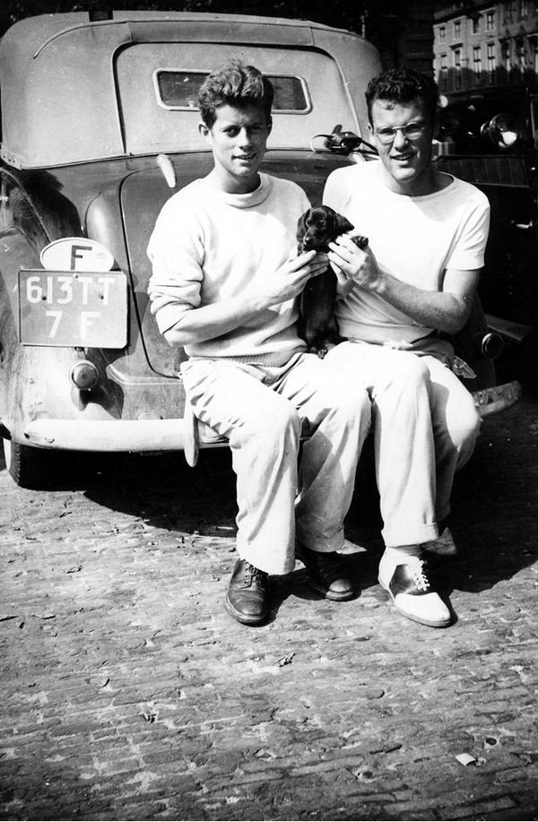 John F. Kennedy and Lem Billings sitting on a car with their Dachshund