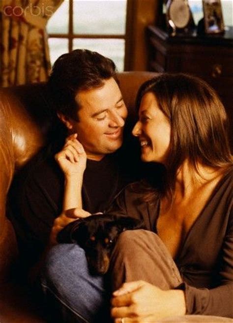 Vince Gill & Amy Grant sitting on the couch with their Dachshund