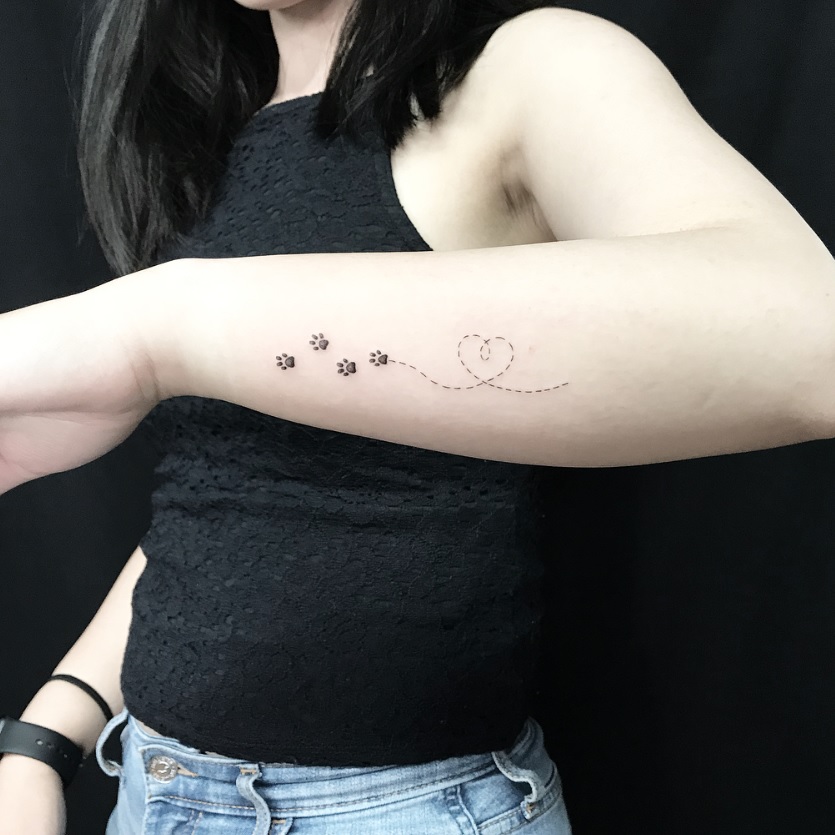 four paw prints with short lines forming a heart behind tattoo on the side of the arms