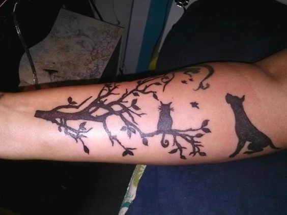 silhouette of a sitting Great Dane facing on the side with a cat sitting on the branch of a tree tattoo on the forearm