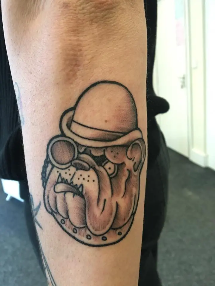 animated English Bulldog wearing one eye glass and a cap tattoo on the forearm