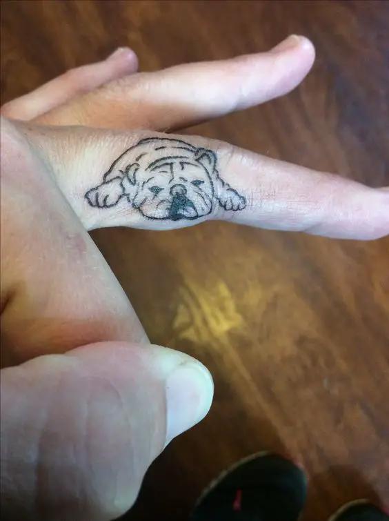minimalist outline of a lying down English Bulldog tattoo on the side of the middle finger