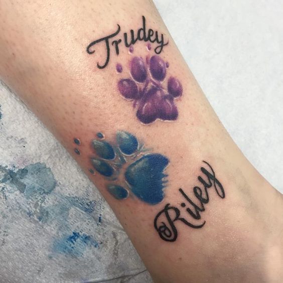 purple and blue colored paw prints with names trudey and riley tattoo on the leg