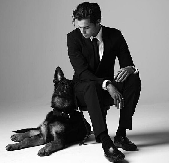 black and white photo of Dylan Rieder sitting on the chair while his German Shepherd is lying down beside him