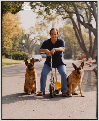 James Belushi sitting on his scooter in between his two German Shepherd sitting on the pavement