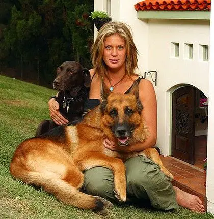 Rachel Hunter sitting on the green grass with her German Shepherd in her lap and a labrador beside her