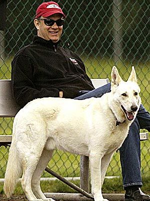Tom Hanks sitting on the bench while his German Shepherd is standing beside him