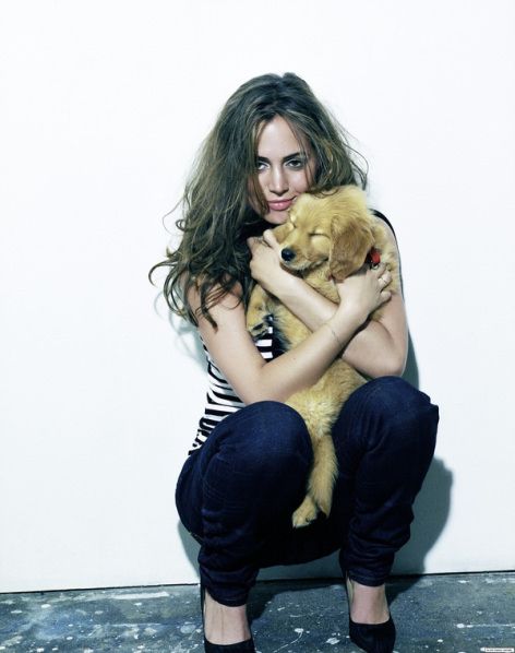 Elisha Dushku sitting on the floor in a white wall while hugging her Golden Retriever puppy