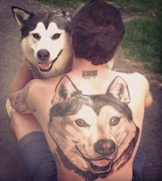 a man sitting on the concrete floor with a face of the Husky he is hugging tattooed on his back