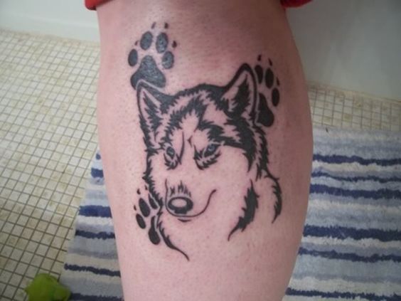 simple tattoo of a husky with two paw print on the leg