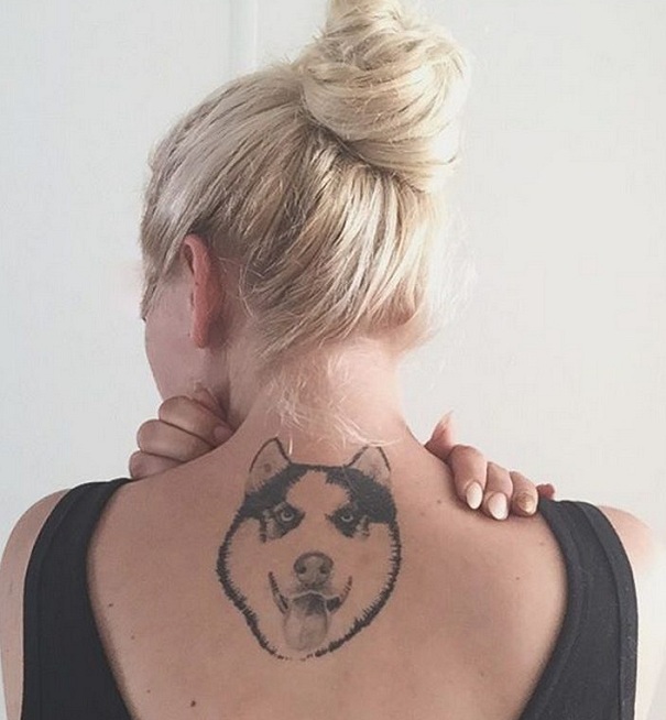 face of a Husky looking up and sticking its tongue out tattoo on the back of a woman