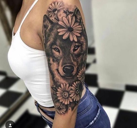 face of a black Husky surround with flowers tattoo on the shoulder of a woman