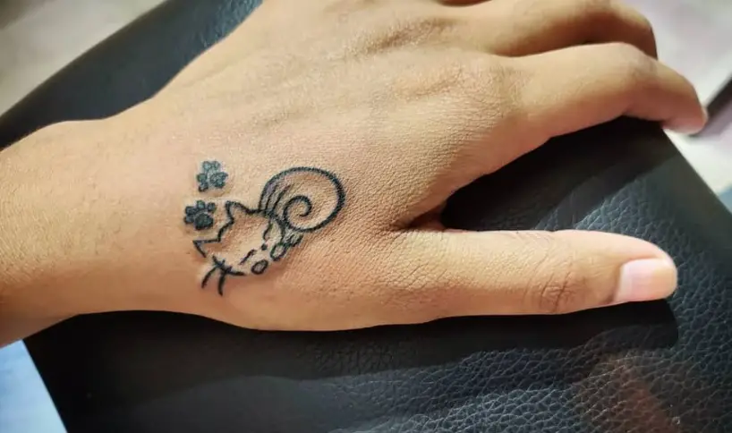 outline of a sleeping cat and a paw print tattoo on the hand