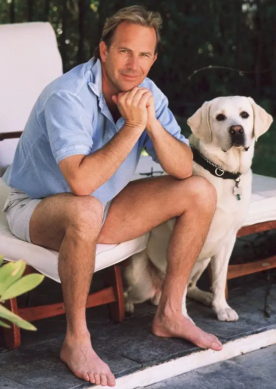 Kevin Costner sitting on the chair with a white Labrador Retriever next to him