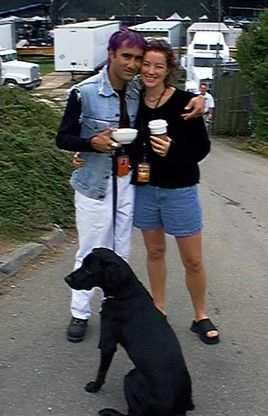 Sarah McLachlan embracing a man while standing with their black Labrador Retriever sitting in front of them