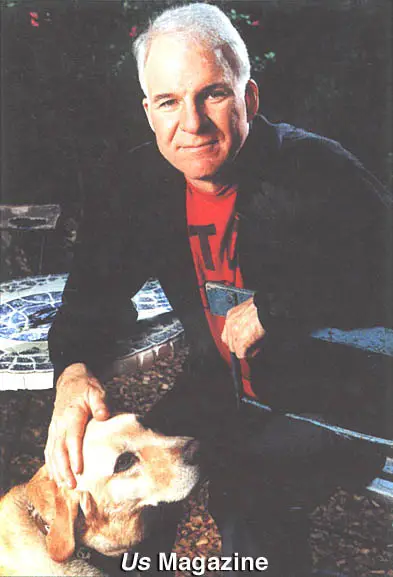 Steve Martin sitting on the bench while petting his Labrador Retriever sitting in front him