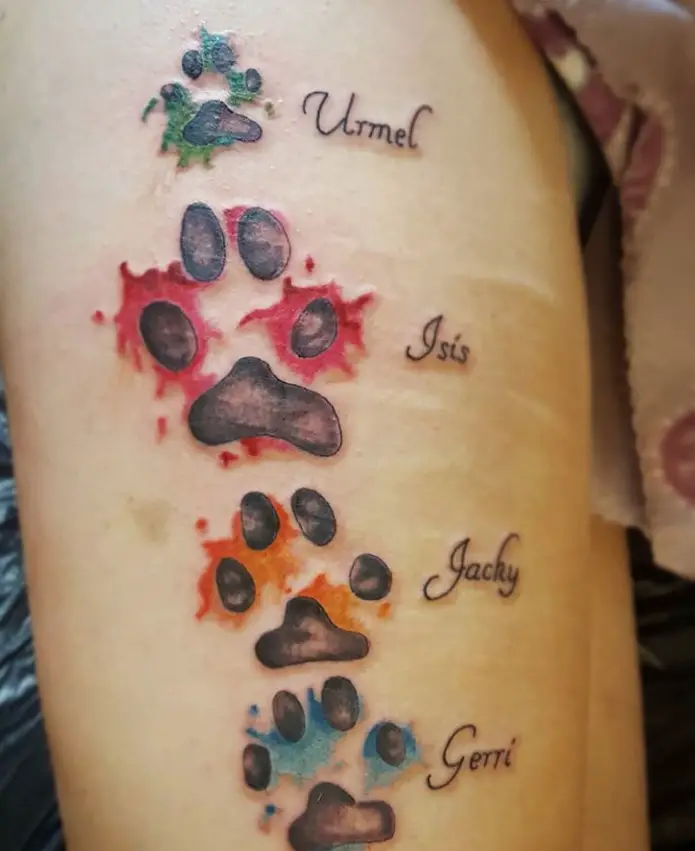 four paw prints with different color and with their names tattoo on the thigh