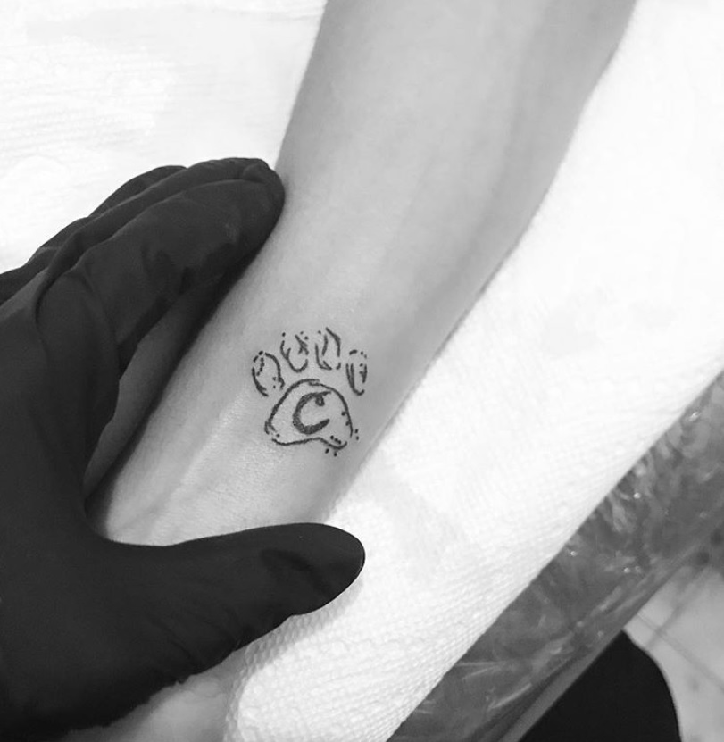 outline of paw print with initial C tattoo on the forearm